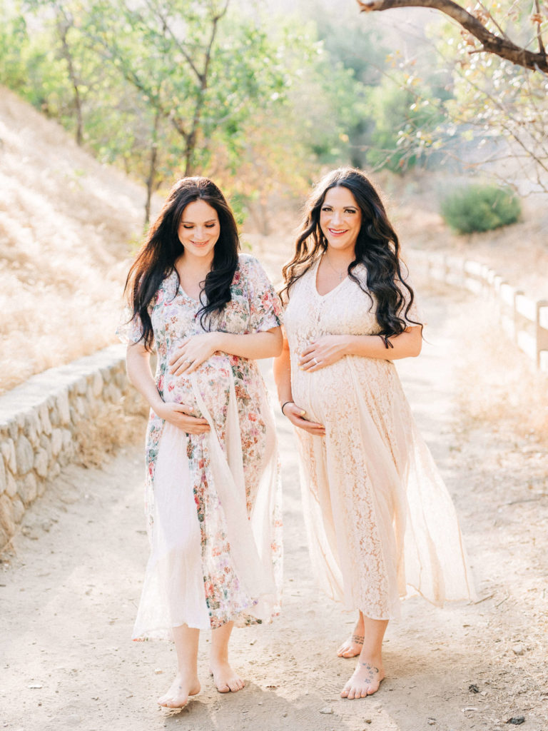 twin pregnant woman holding their bumps while walking
