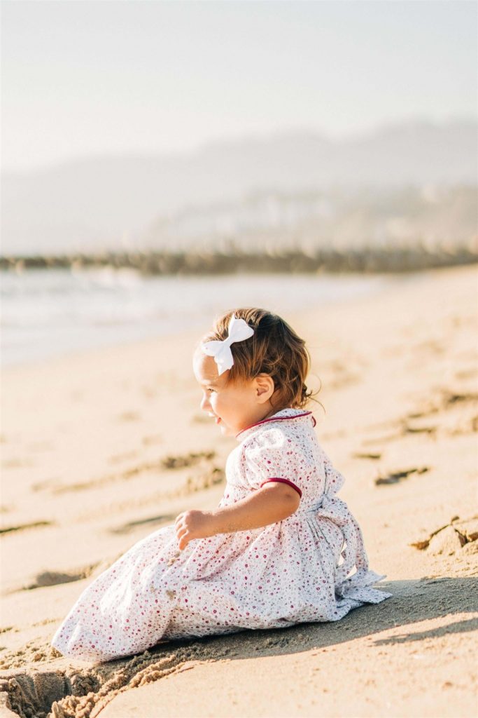 little girl sitting in the sand in a dress from Santa monica baby stores