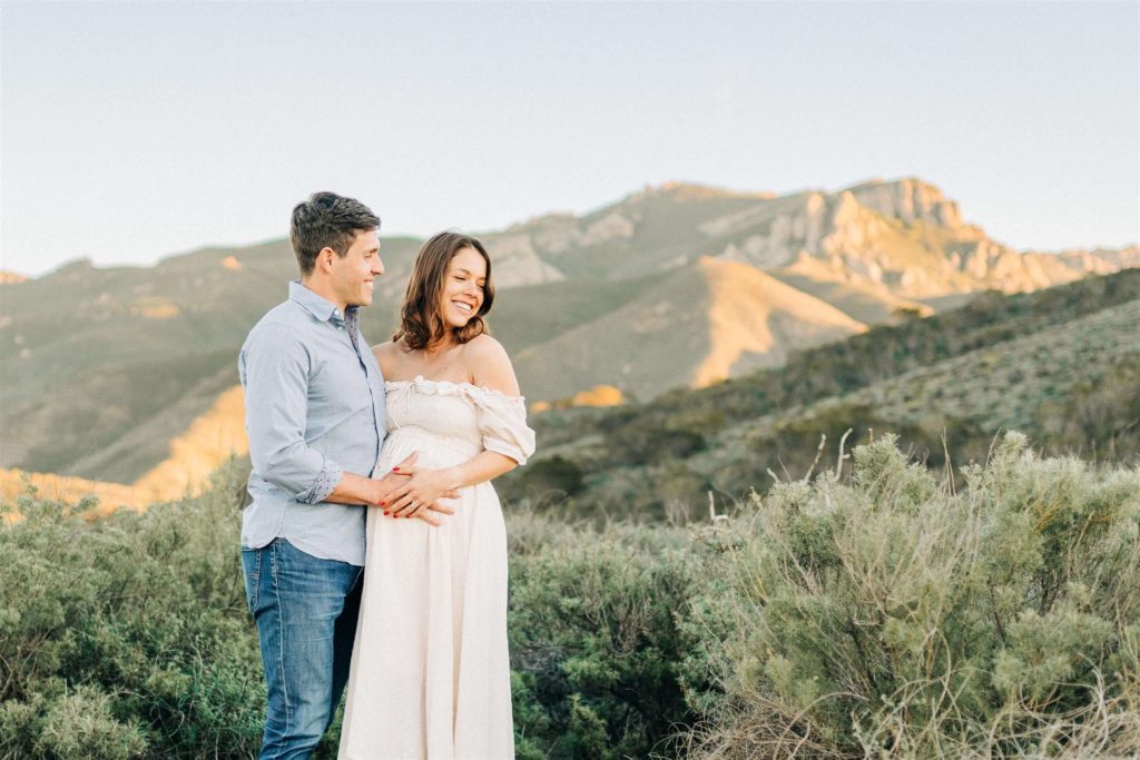 mom to be in cream maternity gown with her husband holding her bump