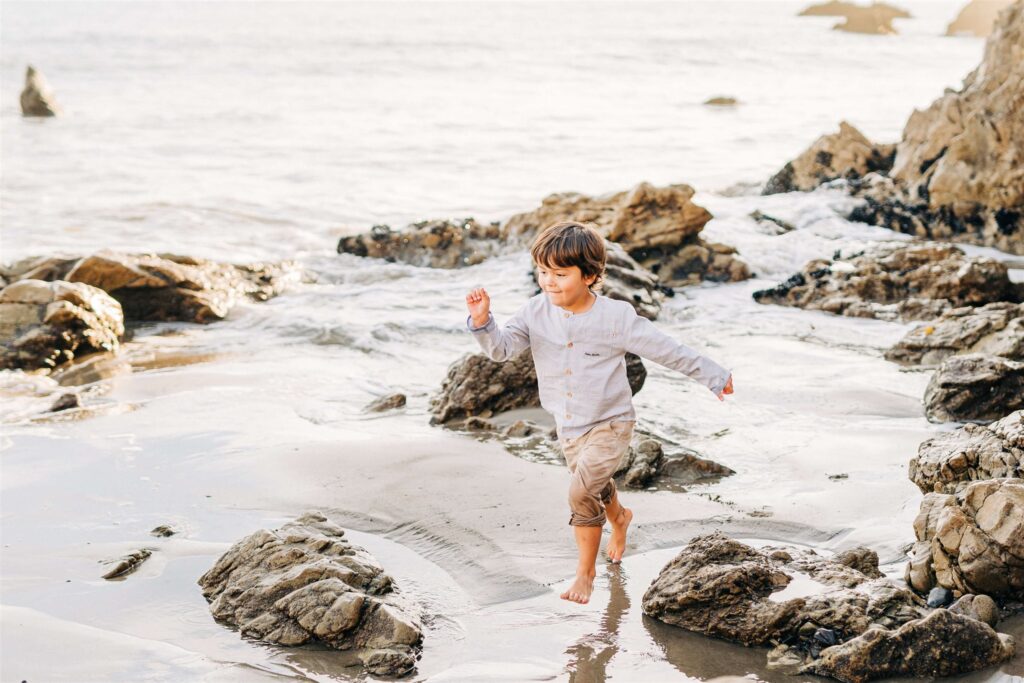 Boy in a grey button-down and khaki pants plays in the rocks on the beach center for early education