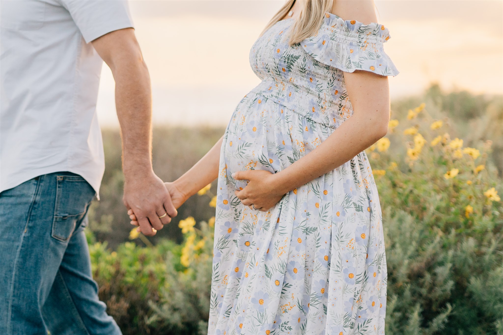 Details of expecting parents holding hands while walking on a beach at sunset